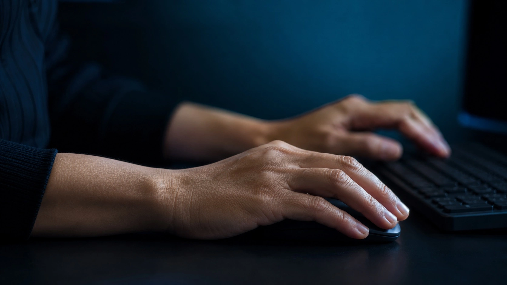 Manos de mujer trabajando con ratón y teclado en la postura mantenida que sobrecarga la muñeca y favorece el síndrome del túnel carpiano